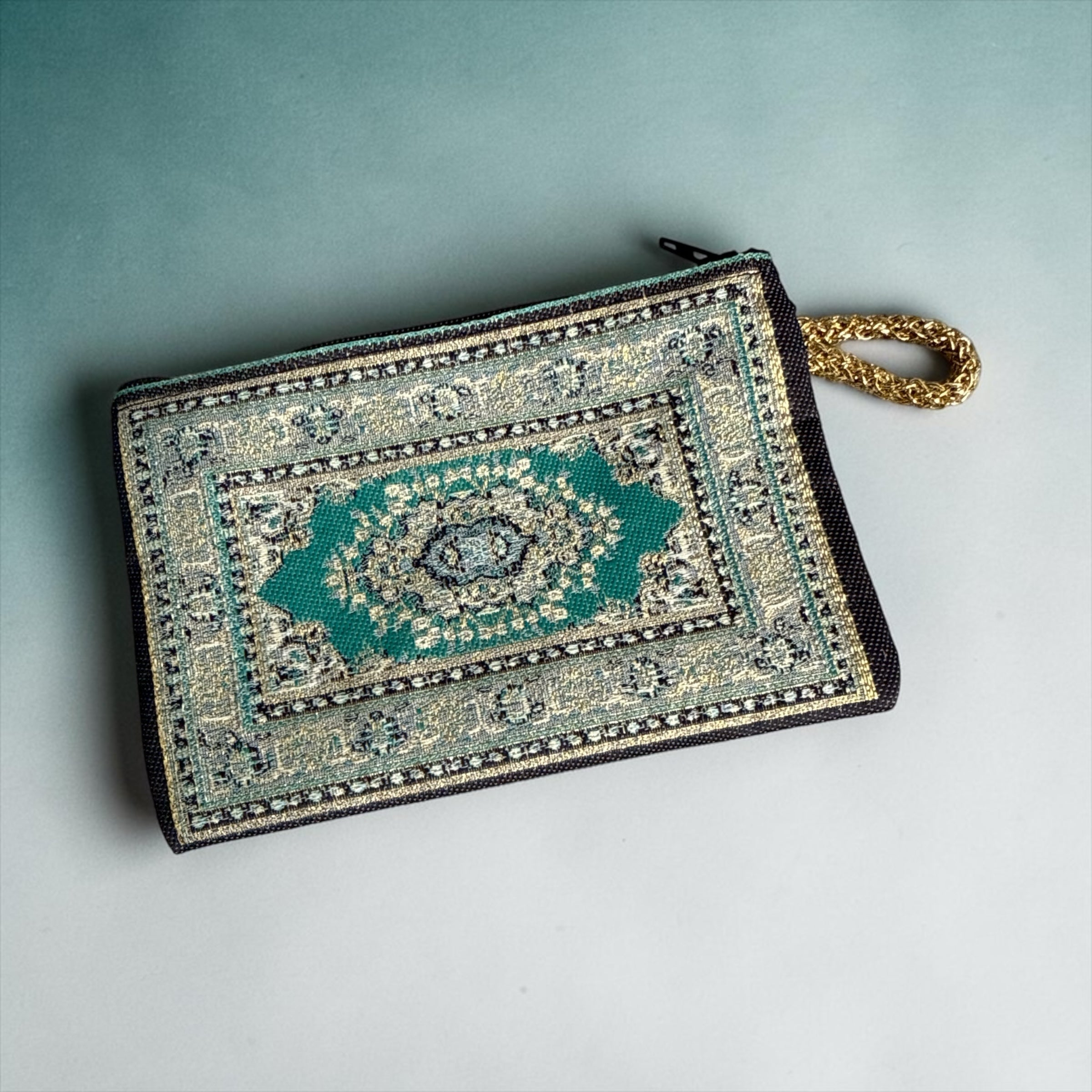 Niomes Boutique teal and gold woven tapestry accessory pouch with a Persian rug pattern and a gold-toned wrist strap.